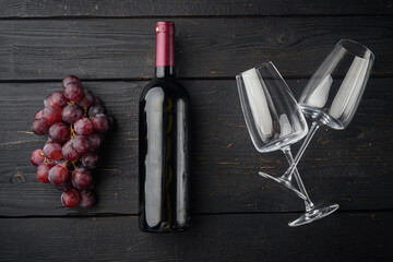 Wine bottle with grapes, on black wooden table background, top view flat lay
