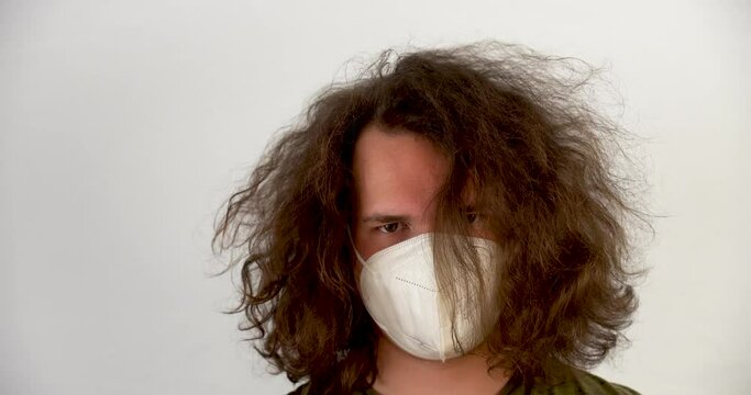 closeup of young blond man in green t-shirt with long hair moving it and is wearing a mask on a white background