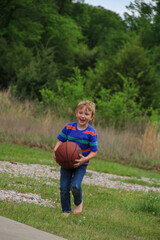 Boy playing with a basketball in the country during spring time