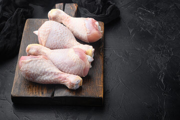 Raw chicken leg quarters, legs meat on bone, on wooden cutting board, on black stone background, with copy space for text