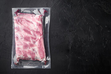 Raw pork ribs vacuum packed, on black stone background, top view flat lay, with copy space for text