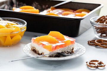 Close up of a slice of peach jelly pretzel dessert ready for eating with a pan of the dessert in behind.