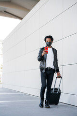 Tourist man using his mobile phone and carrying suitcase outdoors.