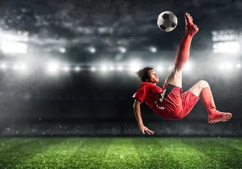 Fototapeten Soccer striker in red uniform hits the ball with an acrobatic kick in the air at the stadium © alphaspirit