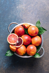 Whole and sliced blood oranges in iron bowl colander on blue table background. Flat lay, top view, copy space.