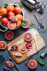 Summer cocktails and fresh orange juice cooking concept. Whole and sliced blood oranges with shaker and bartender utensils over blue table background. Flat lay, top view.