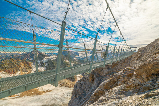Titlis cliff walk suspension bridge on top of Titlis mountain with glacier in the Uri Alps. Viewpoint 3028 m located in cantons of Obwalden and Bern, Switzerland, Europe. Summer season blue cloudy sky