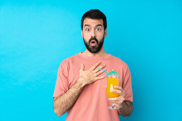 Fototapeta premium Young man over holding a cocktail over isolated blue background surprised and shocked while looking right