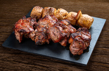 Stone board with different tasty cooked meat on wood background. Pork kebab, potatoes