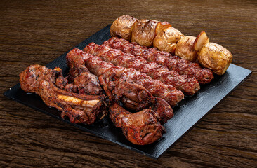 A selection of various barbecued gourmet meats on a black board with a rustic timber background. Rack of lamb, potatoes, kebab