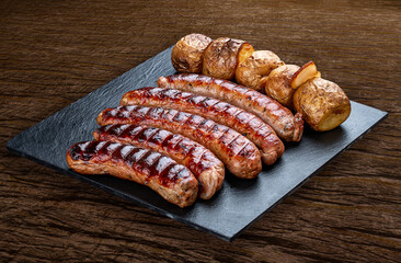 Handmade sausages with baked potatoes on a black board with a rustic timber background.