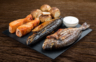 Stone board with different tasty cooked meat on wood background. Assorted meat and fish