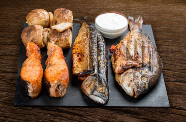 Stone board with different tasty cooked meat on wood background. Assorted meat and fish