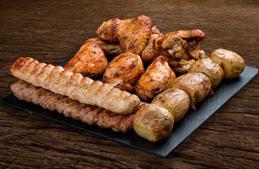 Stone board with different tasty cooked meat on wood background. Assorted meat
