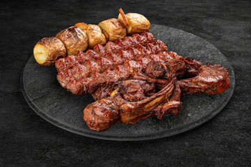 A selection of various barbecued gourmet meats on a black board with a rustic timber background. Rack of lamb, potatoes, kebab