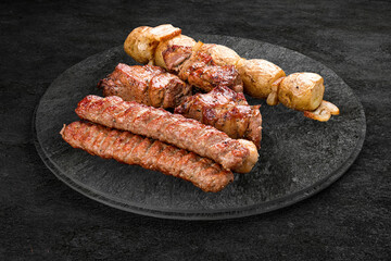 A selection of grilled gourmet meats on a rustic stone board. Chicken kebab and pork.