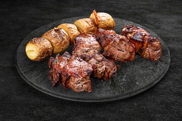 A selection of grilled gourmet meats on a rustic stone board. Pork kebab with abked potatoes