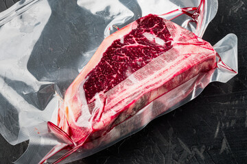 Fresh marbled meat black angus steak in vacuum plastic bag for sous vide, on black stone background - obrazy, fototapety, plakaty