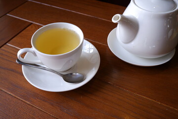 White teapot and a cup of green tea on a wooden background.