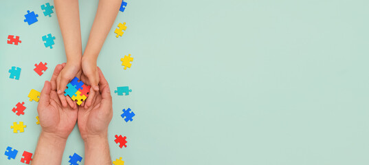 World autism awareness day. Understanding - love concept. The hands of an autistic father and child hold a colorful puzzle on blue background. ASD. Heart of puzzles.Copy space. Banner. Layout