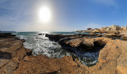 Fototapeta na wymiar Waves crashing on rocks. Salt production. Discover the world. Heavy wind at the beach. Place to relax and enjoy tanning. Vacations in Lebanon. Sunset panoramic image