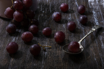 Ripe juicy red grapes with berries and a vintage spoon on a wooden table. Still life in a dark mood.