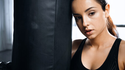 tired young sportswoman leaning on punching bag in gym.