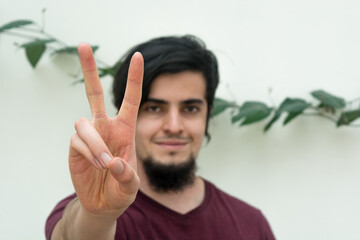 Portrait of a young caucasian black haired man with beard and red shirt looking at camera and smiling naturally, confident and friendly. White background and climbing plant with leaves behind