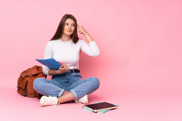 Teenager caucasian student girl sitting on the floor isolated on pink background with problems making suicide gesture