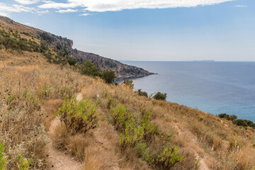 A path among dry grass on a mountainside descending to the sea, Albania