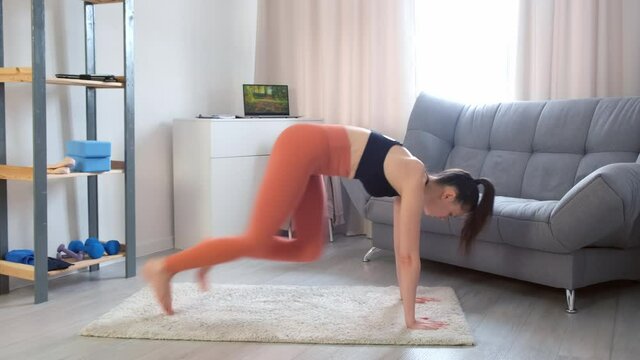 Young woman making plank flexing legs exercise in dynamic at home, side view. Sporty fit female doing fitness aerobic cardio exercises. Home workout, training and wellness concept.