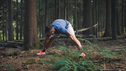 Wide shot of Caucasian man in sportswear doing legs and back stretching exercises in the forest