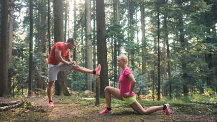 Naklejka na ściany i meble Caucasian woman and man in sportswear doing post run leg stretching exercises in the forest