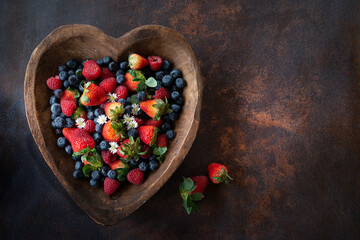 Assorted fresh berries in a heart-shaped wooden bowl