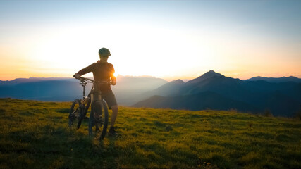 Woman walking uphill with mountain bike at a sunset.