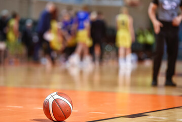 Basketball ball on the parquet with team and referee in the background.