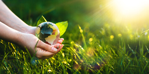 Hands holding crystal earth globe in sunny green grass.  Environment, save clean planet, ecology...