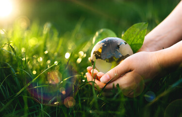 Hands holding crystal earth globe in sunny green grass.  Environment, save clean planet, ecology...