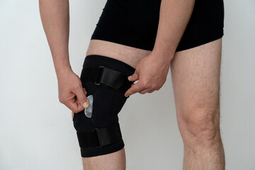 Leg support. A man adjusts a black orthosis on his leg. Copspace - Powered by Adobe