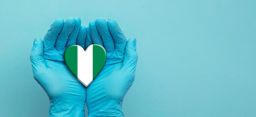Doctors hands wearing surgical gloves holding Nigeria flag heart