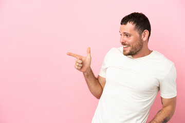 Young Brazilian man isolated on pink background pointing finger to the side and presenting a product