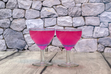 Two glasses of pink cocktail with gas bubbles close-up against the background of unfolded stone wall