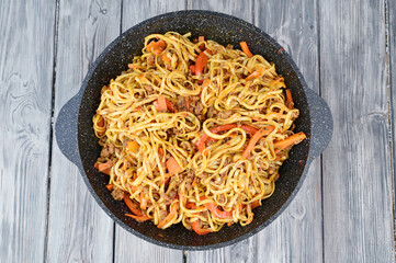 Top view of a wok pan with udon noodles. Pieces of red bell pepper and carrots are visible
