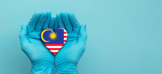 Doctors hands wearing surgical gloves holding Malaysia flag heart