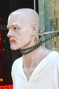 Tied by neck damaged, aggressive looking male manikin with white shirt on the street; color photo.
