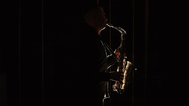 Black silhouette of male saxophonist musician playing golden alt saxophone on musical instrument. Cool saxophone player performing a solo on stage. Musician playing in band