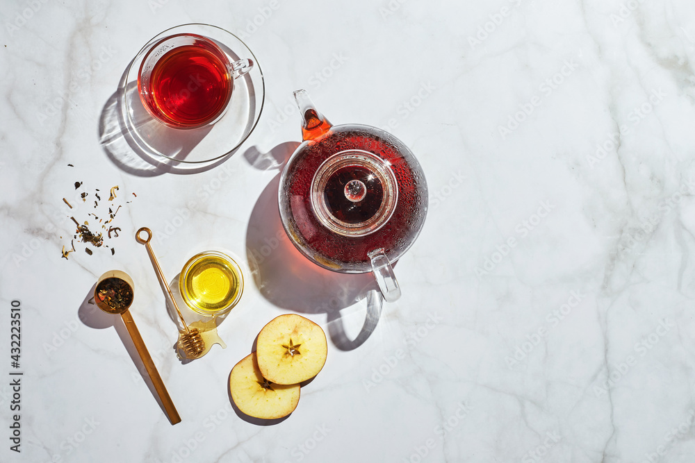 Wall mural fruit tea with apples and thyme and honey in glass teapot and cup on white background with hard shad