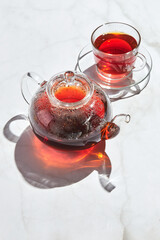 Fruit tea with apples and thyme and honey in glass teapot and cup on white background with hard shadows