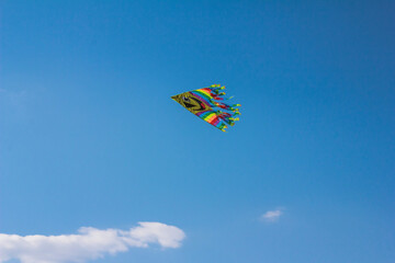Bright yellow kite with smiles flying in the blue sky over the clouds. Copy space, stock photo