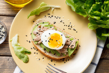 Avocado, canned tuna and boiled egg toast on wooden table background. Healthy food, avocado open sandwich for breakfast or lunch. Flat lay, top view, close up